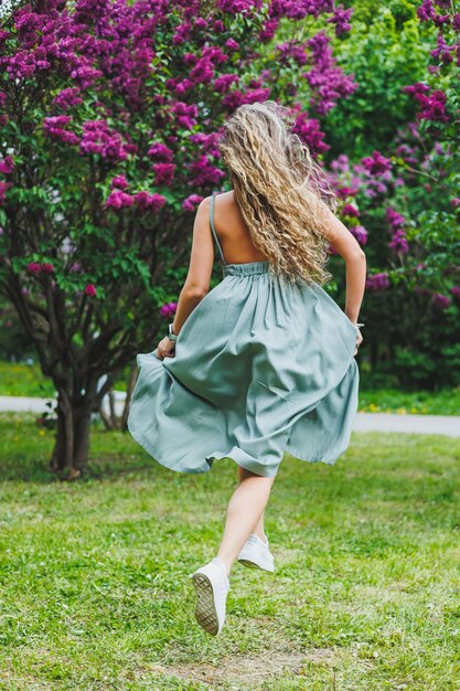 Une belle femme bouclée dans une robe d'été court et se réjouit qu'elle porte des lunettes de soleil sur fond d'un buisson de lilas violet