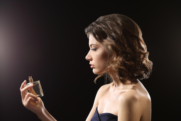 Belle femme avec une bouteille de parfum sur fond sombre