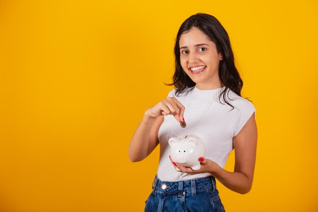 Belle femme brésilienne tenant une tirelire et une pièce de monnaie