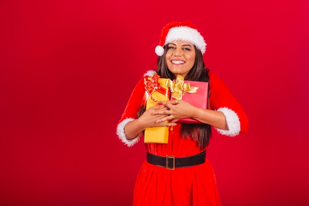 Belle femme brésilienne vêtue de vêtements de Noël Père Noël étreignant deux cadeaux