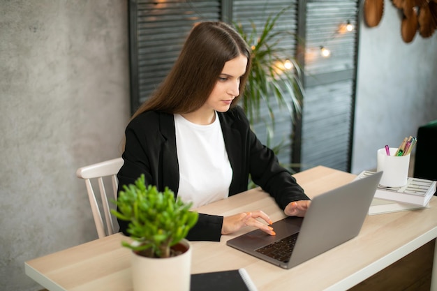 Belle femme brune à l'aide d'un ordinateur portable au bureau chic