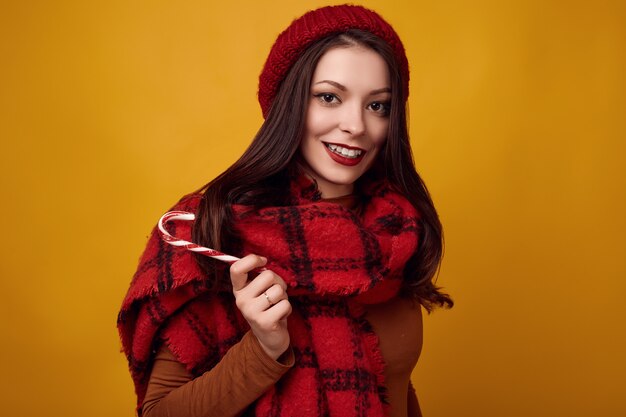 Belle femme brune au chapeau rouge avec une grande écharpe tricotée tenant un bonbon