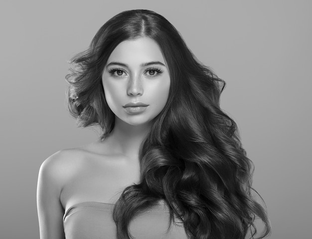 Belle femme brune aux cheveux longs et bouclés avec un maquillage de beauté et un portrait de la mode féminine de la peau saine. Prise de vue en studio. Monochrome gris noir et blanc.