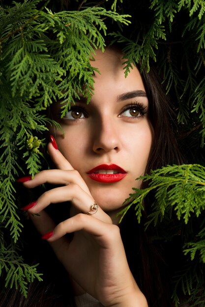 Belle femme brune aux lèvres rouges posant sur fond de thuya