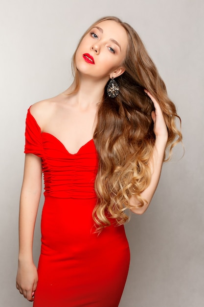 Belle femme brune aux longs cheveux bouclés dans une robe rouge portant des boucles d'oreilles.