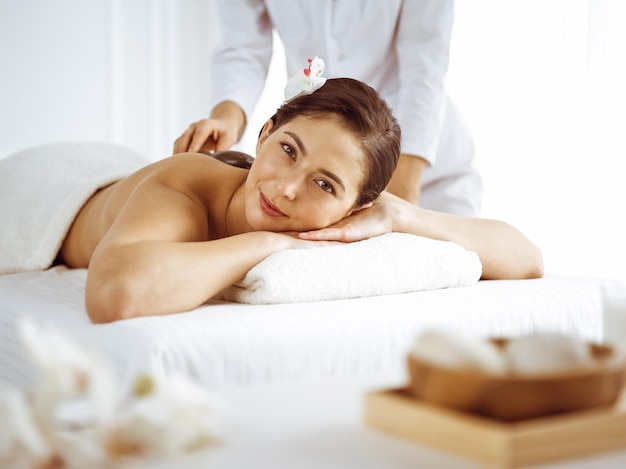 Belle femme brune bénéficiant d'un massage du dos avec les yeux fermés. Concept de spa et de médecine.