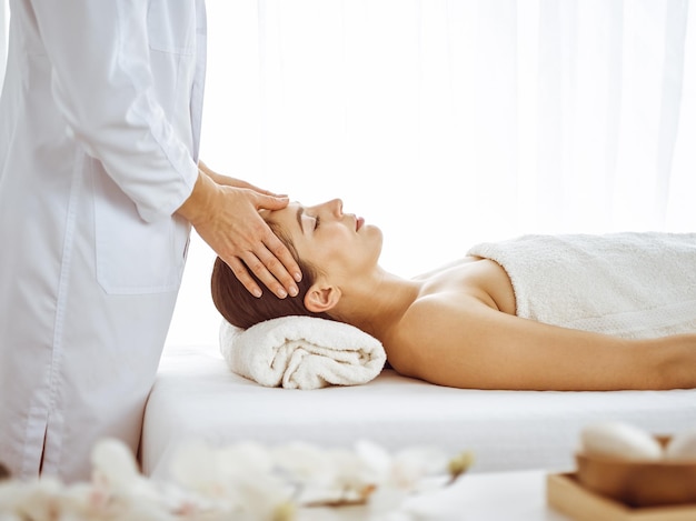 Belle femme brune bénéficiant d'un massage facial avec les yeux fermés. Traitement relaxant dans les concepts de centre de médecine et de spa.