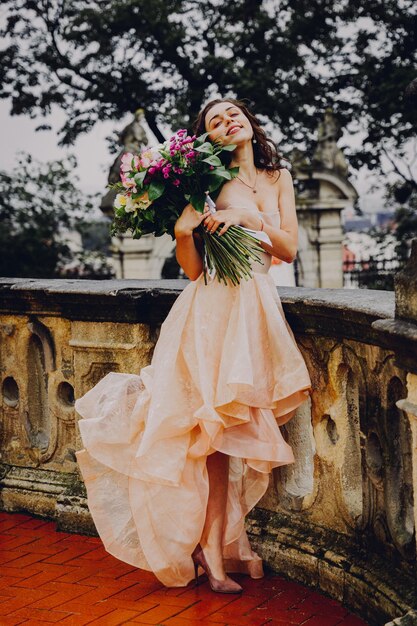 Belle femme brune avec un bouquet de fleurs dans une robe rose