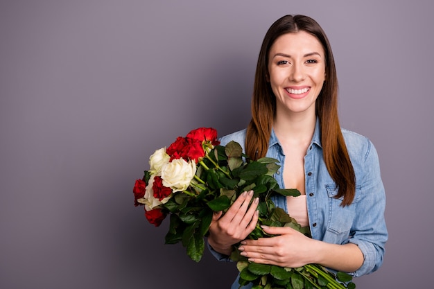 Belle femme brune en chemise de jeans posant avec bouquet contre le mur violet