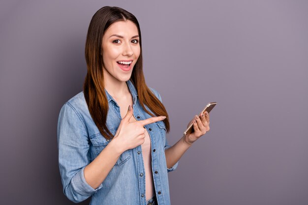 Belle femme brune en chemise de jeans posant avec son téléphone contre le mur violet