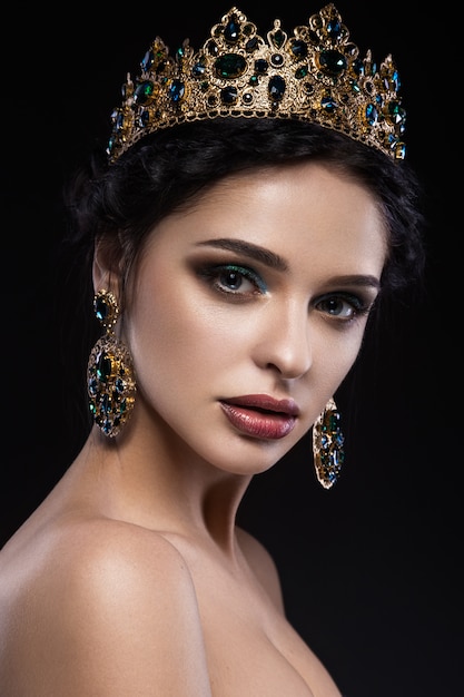 Belle femme brune avec une couronne d'or, des boucles d'oreilles et du maquillage de soirée professionnel