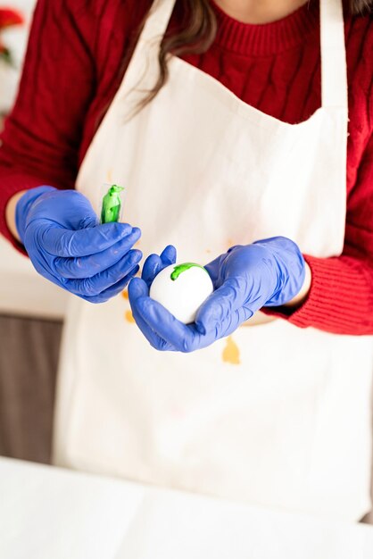 Une belle femme brune dans un pull rouge et un tablier blanc colorant des œufs de Pâques dans la cuisine