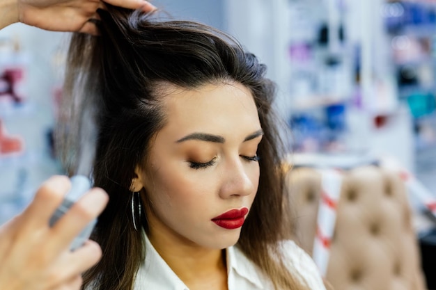 Une belle femme brune est vaporisée sur ses cheveux dans un salon de beauté.