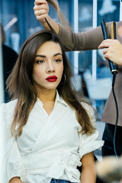 Belle femme brune a un fer à repasser dans un salon de beauté.