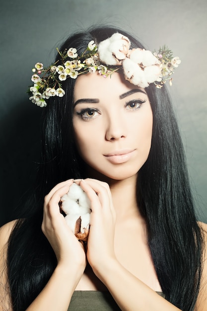 Belle femme brune avec des fleurs de coton dans les cheveux et la main. Photo de mode