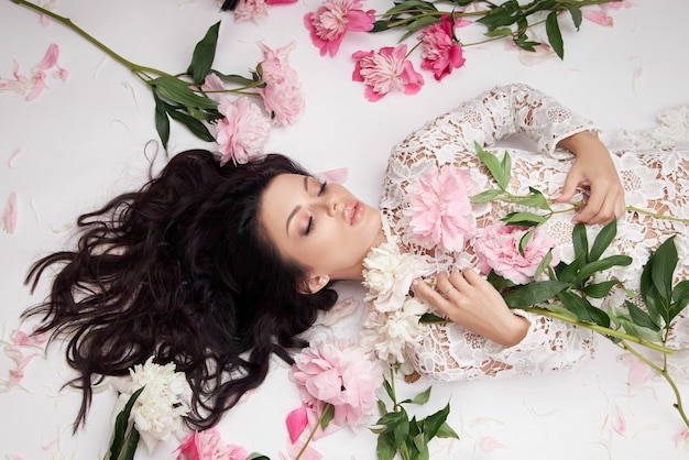 Belle femme brune avec des fleurs de pivoine. Cosmétiques et maquillage naturels, peau parfaite