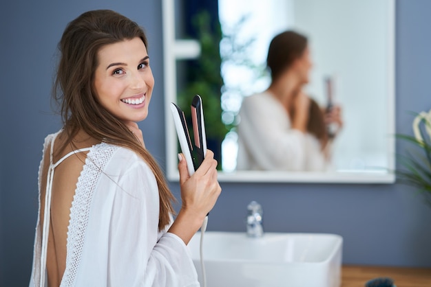 Belle femme brune lissant les cheveux dans la salle de bain