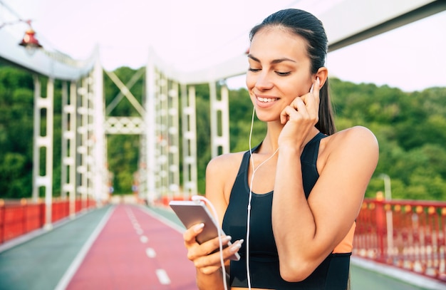 Belle femme brune mince sportive dans des vêtements de sport et des écouteurs sur des exercices du matin à l'extérieur