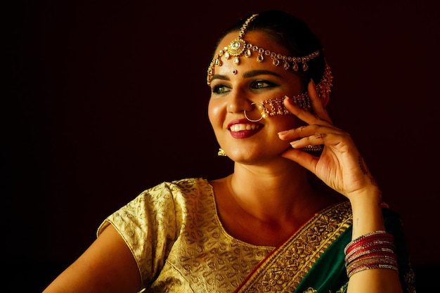 Belle femme brune de mode indienne en sari riche de mariage traditionnel vert avec des bijoux en or anneau de nez piercing nath mis en maquillage professionnel sur fond noir foncé