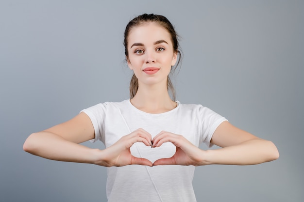 Belle femme brune montrant le coeur avec les mains isolées sur gris