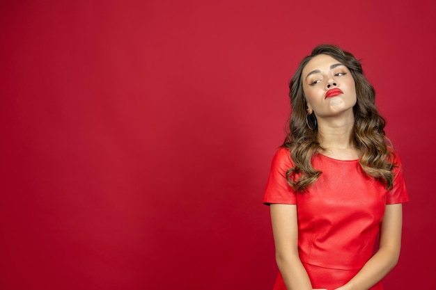 Belle femme brune offensée en robe rouge sur fond rouge avec espace de copie