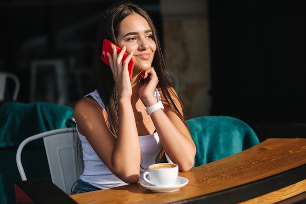 Belle femme brune parlant au téléphone dans le café à proximité d'une femme utilisant un téléphone