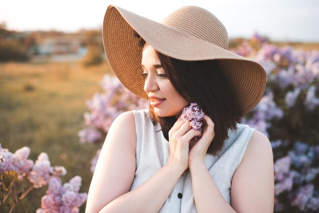 Belle femme brune porte un chapeau de paille tenant une fleur lilas sur la nature