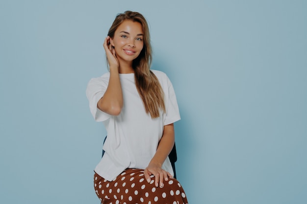 Belle femme brune porte un t-shirt décontracté blanc et une jupe qui pose en studio