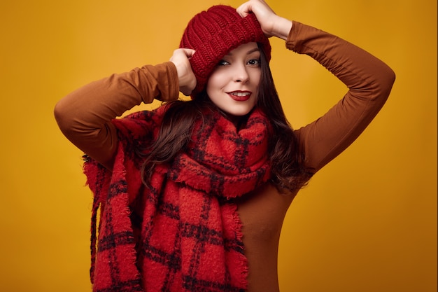 Belle femme brune en pull et bonnet rouge avec une grande écharpe tricotée