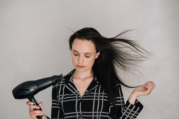 Photo belle femme brune en pyjama noir séchant les cheveux