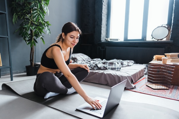 Belle Femme Brune De Remise En Forme Faire Des Exercices D'étirement Devant Un Ordinateur Portable, Faire Du Yoga à L'intérieur à La Maison