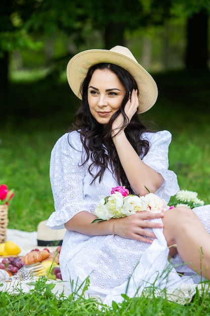 Belle femme brune se reposant dans un parc assis sur une couverture de pique-nique se détendre dans la nature