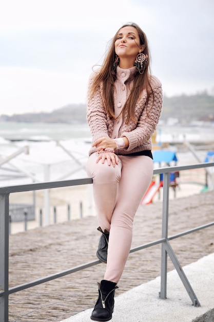 Belle femme brune souriante assise sur une clôture en face de la plage de la ville