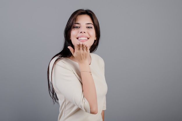 Belle femme brune souriante envoie un baiser isolé sur gris