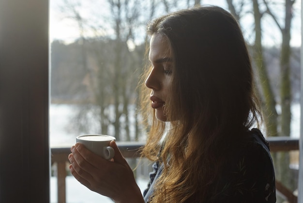 Belle femme buvant du café le matin assis près de la fenêtre. vue de l'extérieur.