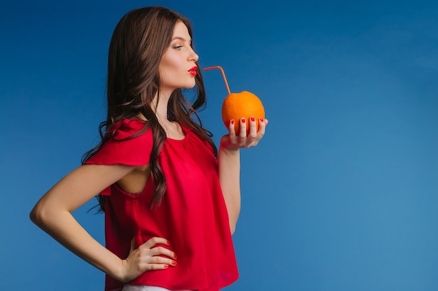 Belle femme buvant du jus d'orange naturel directement de l'orange à travers une paille