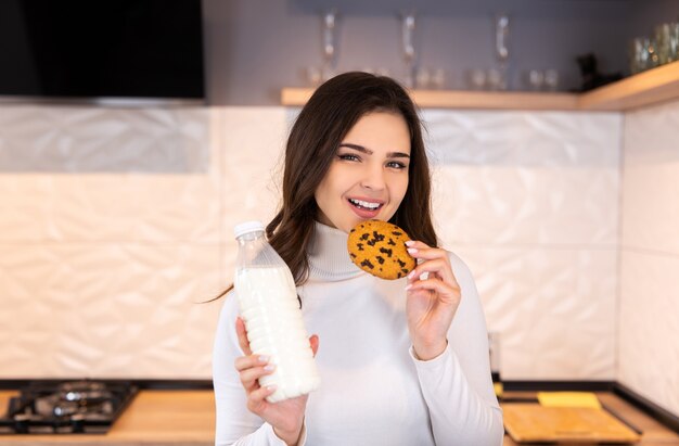 Belle femme buvant du lait savoureux avec des biscuits dans la cuisine à la maison.