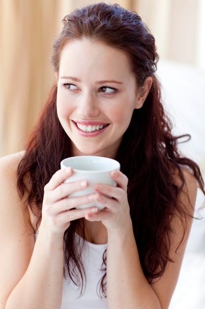 Belle femme buvant une tasse de café au lit