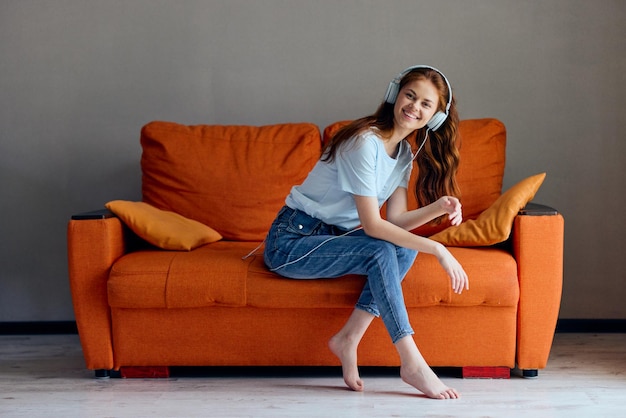 Belle femme sur le canapé orange écoutant de la musique avec des technologies d'écouteurs