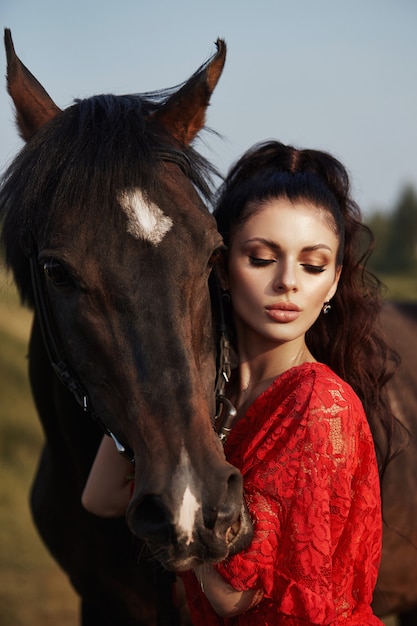 belle femme caresse un cheval et tient la bride dans un champ