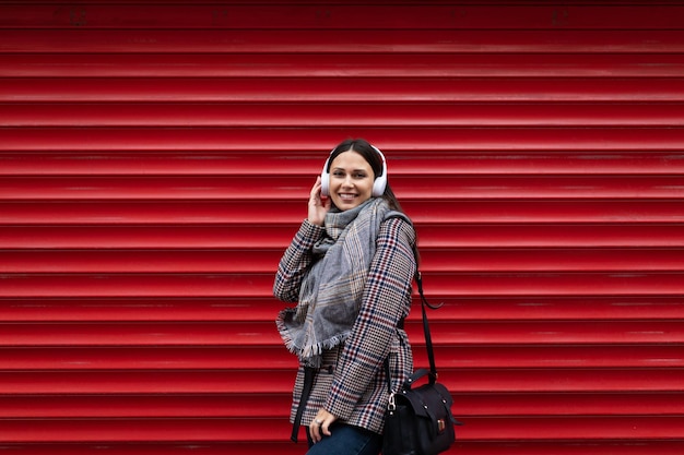 Belle femme caucasienne adulte dans des écouteurs avec un sourire sur le fond d'un mur rouge en relief