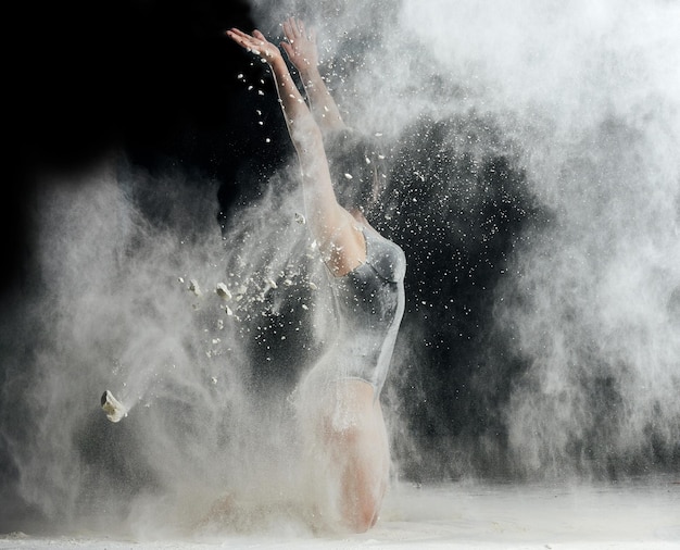 Photo une belle femme caucasienne en costume noir avec une figure sportive danse dans un nuage blanc de