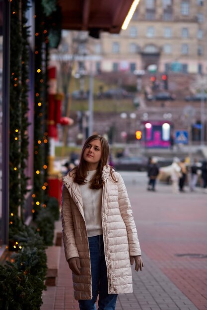 Belle femme caucasienne dans la rue près de la vitrine décorée Vêtements décontractés d'hiver élégants Ville festive Lumières du soir de la ville