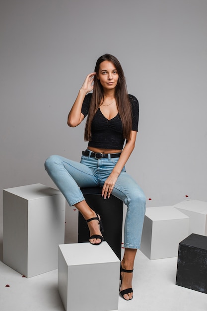 Belle femme caucasienne est assise sur un cubes blancs et regarde, photo isolée sur un mur blanc