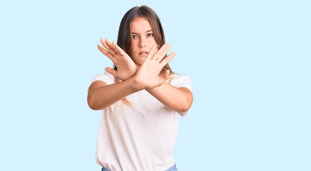 Belle femme caucasienne portant une expression de rejet de t-shirt blanc décontracté croisant les bras faisant signe négatif, visage en colère