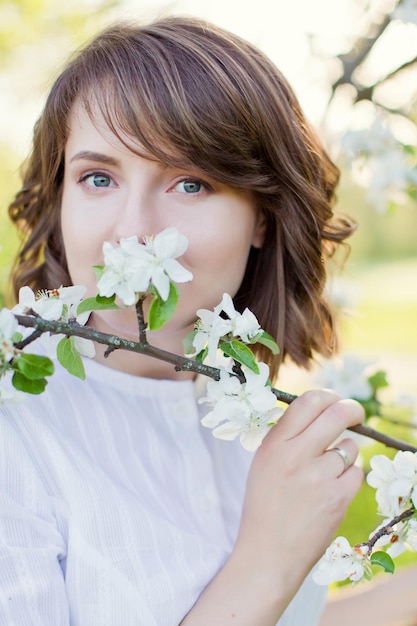 Belle femme caucasienne en robe blanche se promène dans le jardin de fleurs de printemps