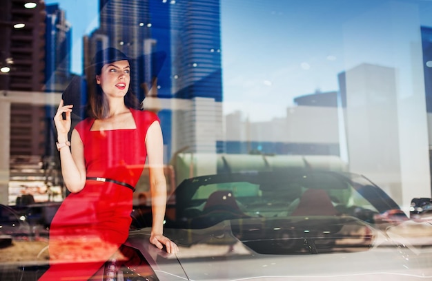 Belle femme caucasienne en robe rouge avec une voiture de luxe