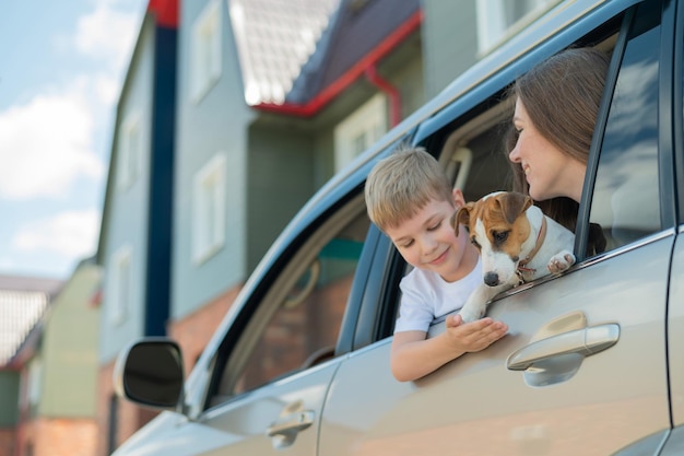 Belle femme caucasienne voyage avec un enfant et un chien Maman et son fils se sont penchés par la fenêtre de la voiture dans une étreinte avec un chiot de Jack Russell Terrier Une famille heureuse part en voyage en voiture