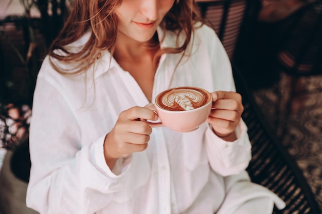 Belle femme en chemise blanche boire un cappuccino avec un latte art au café