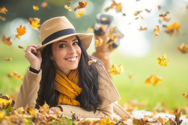 Une belle femme coiffée d'un chapeau se couche dans la nature entourée de feuillage.